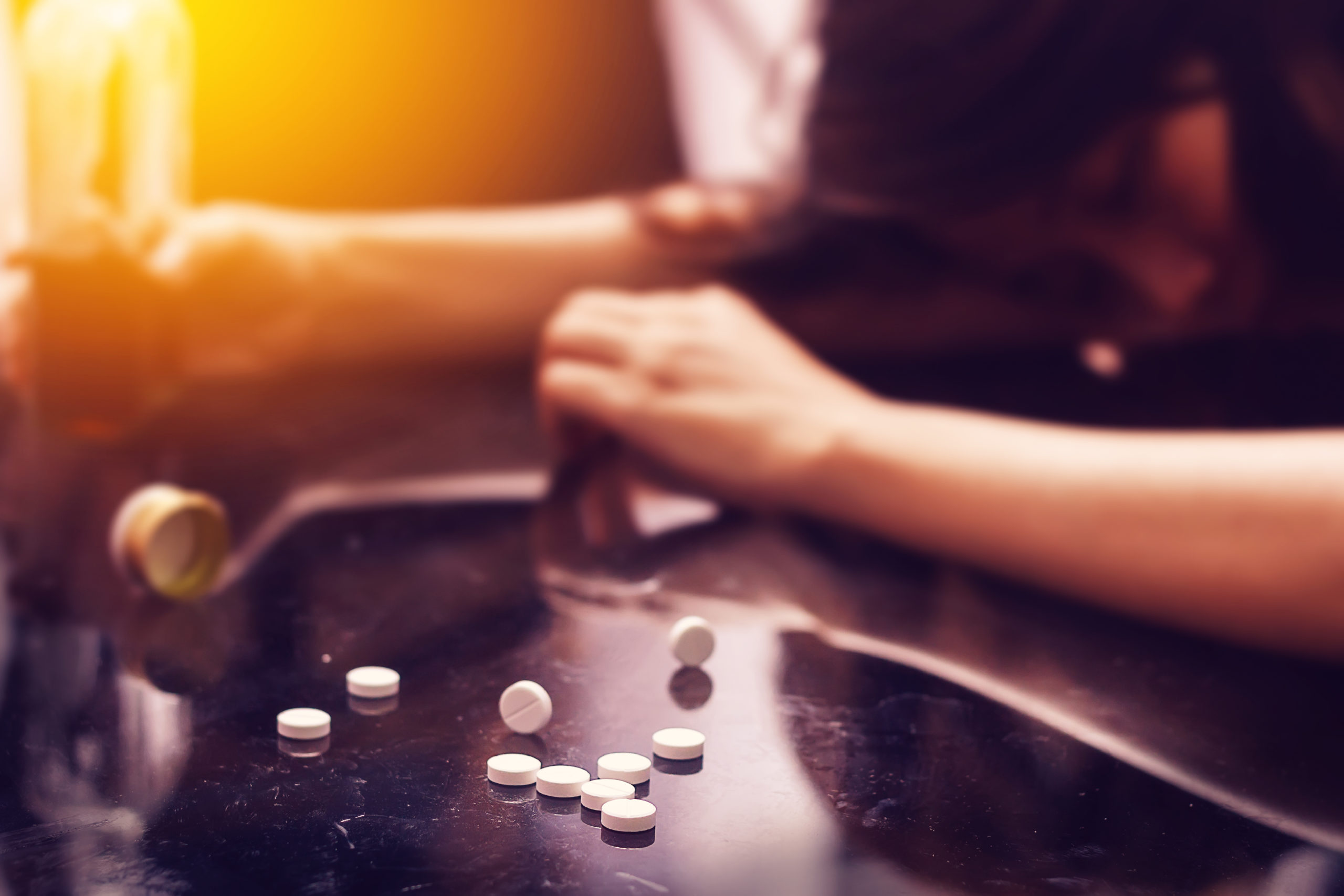 Arms on table, there are opioid pills scattered across the table